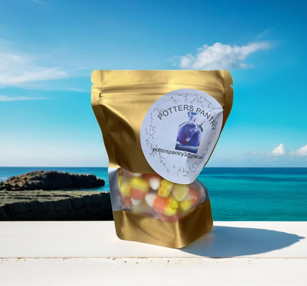 A gold resealable bag labeled "Potter's Pantry" with assorted Dehydrated sweets candies inside. The bag is placed on a glass surface with a clear ocean view in the background.