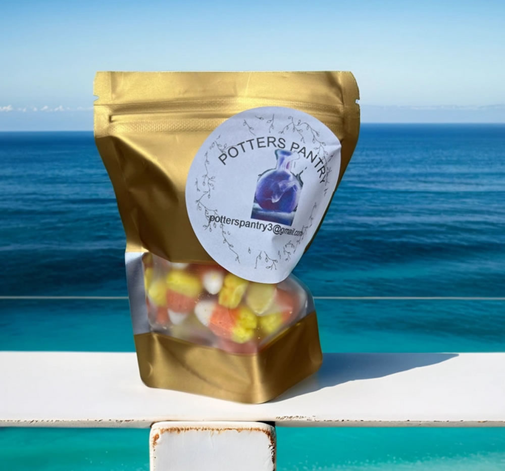 A gold resealable bag labeled "Potter's Pantry" with assorted candies inside. The bag is placed on a glass surface with a clear ocean view in the background.